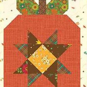 May include: A patchwork quilt block with a pumpkin design. The pumpkin is mainly orange with a starburst pattern in the centre, using brown, yellow, and floral fabrics. The top and bottom borders have patterned fabric strips.