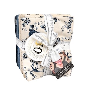 Puede incluir: Un conjunto de cuadrados de tela, color crema con un diseño floral y de pájaros azul, atados con una cinta impresa con medidas y el texto "FABRICS". Una etiqueta con el texto "moda FABRICS + SUPPLIES" está adjunta.