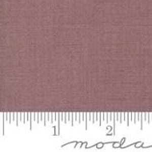 May include: A close-up of a dusty rose fabric with a subtle woven texture. The fabric is displayed with a ruler showing measurements in inches. The word "moda" is printed in cursive at the bottom.