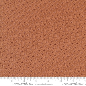 May include: A fabric with a small, repeating pattern of brown leaves on a light orange background. The fabric is measured with a ruler in inches.
