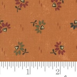 May include: Close-up of a fabric with a repeating floral pattern. The flowers are in shades of burgundy, green, and blue, with a yellow center. The background is a solid orange-brown color. A ruler is at the bottom, showing measurements in inches.