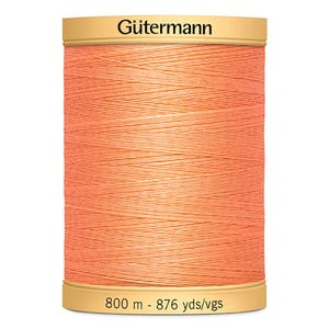 May include: A spool of Gütermann thread in a light peach colour. The spool has a gold-coloured top and bottom with the brand name "Gütermann" printed on the top. The spool contains 800 metres of thread.