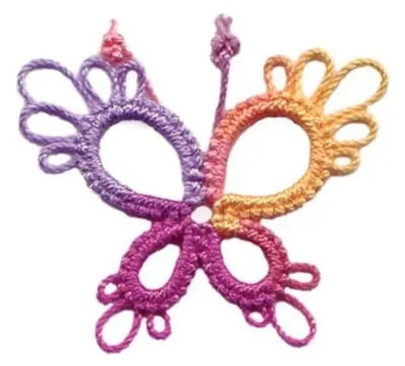 Op de afbeelding: Een gehaakte vlinder van paars, roze en oranje garen. De vlinder heeft een delicaat, ingewikkeld ontwerp met meerdere lussen en bochten.