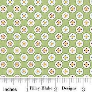 May include: Green fabric with a repeating pattern of white circles with small colored dots inside. The circles are arranged in a diagonal pattern.