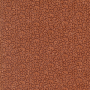 May include: A close-up of fabric featuring a repeating pattern of dark brown, swirling, star-like shapes on a warm, reddish-brown background. The fabric has a textured appearance, possibly woven.