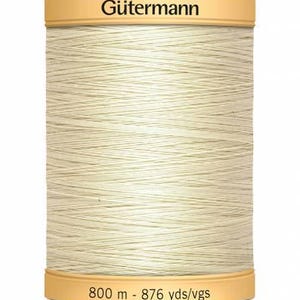 May include: A cream-coloured spool of Gütermann thread, with beige labels at the top and bottom. The bottom label reads "800 m - 876 yds/vgs". The spool is filled with tightly wound thread, suitable for sewing and craft projects.