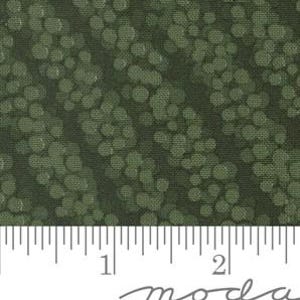 Op de afbeelding: Een donker olijfgroene stof met een herhalend patroon van lichtgroene ronde stippen in diagonale strepen. Een witte liniaal onderaan de afbeelding toont een schaal van vijf centimeter als referentie voor de afmetingen.