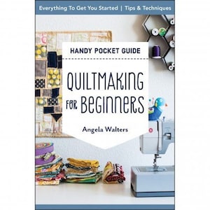 May include: A book cover with the title "Quiltmaking for Beginners" in a white rectangle with a black border. The book cover is a handy pocket guide and features a colorful quilt, a sewing machine, and fabric scraps.