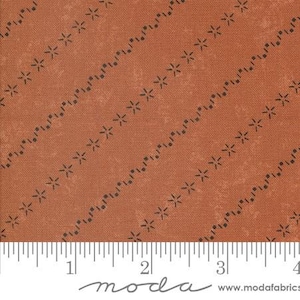 May include: A close-up of a rust-coloured fabric with a black zig-zag pattern and small black stars. The fabric is measured with a ruler in inches.
