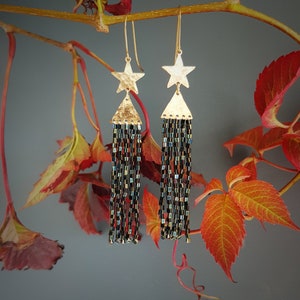 Könnte beinhalten: Goldene Ohrringe in Sternform mit schwarzen und schillernden Perlenfransen.