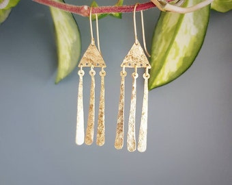 May include: Gold triangle dangle earrings with three thin, textured, gold bars hanging from each triangle.