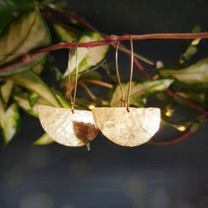 May include: A pair of gold-toned earrings with a hammered, half-circle design. The earrings are suspended from thin, gold-toned wires.