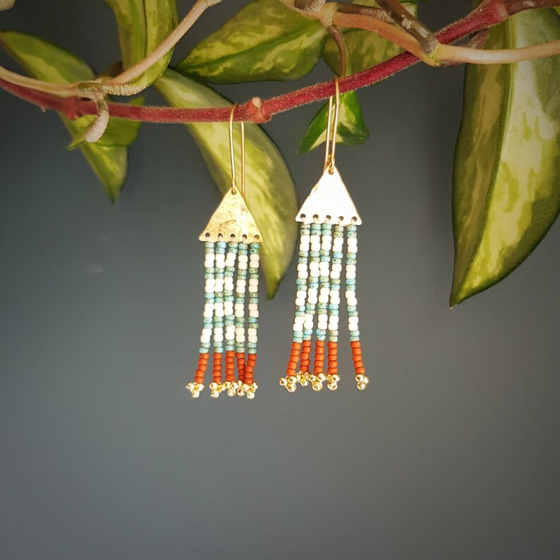 May include: Gold triangle dangle earrings with white and turquoise beads and red beads at the bottom.