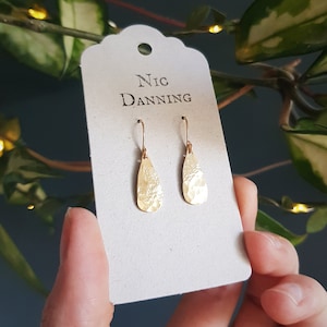 Può includere: Orecchini a goccia d'oro con una texture martellata, esposti su una carta con il testo "Nic Danning".