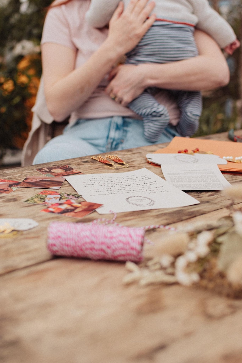 May include: A wooden table displays stationery items, including printed cards, envelopes, and a roll of pink and white twine. The scene is illuminated by natural light, suggesting a craft or stationery theme.
