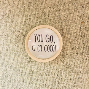 May include: White oval-shaped button with a black border and the text "You go, Glen Coco!" printed in black.