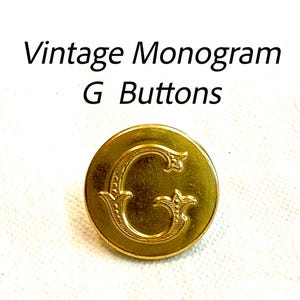 May include: A gold-colored button with the letter "G" in an ornate, vintage style. The button is round and has a shiny finish. Text above the button reads "Vintage Monogram G Buttons".