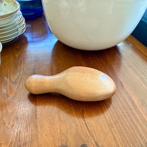 May include: A light-colored wooden shoe stretcher, designed to maintain the shape and fit of footwear. The stretcher has a rounded head and a handle, and is made of smooth, unfinished wood. It is a tool for shoe care and maintenance.