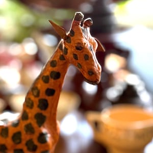 May include: A handcrafted giraffe figurine with a long neck and distinctive black spots on an orange-brown body. The giraffe has detailed features and is likely made of a paper-based material. The figurine is a decorative item.