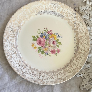 Könnte beinhalten: Ein vintage weißer Keramik-Dinnerteller mit goldfarbenem Rand und einem Blumendesign. Der Teller zeigt einen Strauß aus rosa, gelben und blauen Blumen mit grünen Blättern.