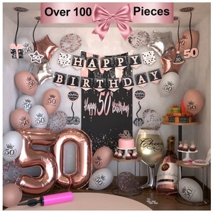 Op de afbeelding: Een decoratieset voor een 50e verjaardagsfeest met roze gouden en zwarte accenten. De set bevat ballonnen, banners, confetti, een taart en een fles champagne. De banner luidt "Happy Birthday".