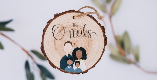 A hand-painted wooden Christmas ornament with a personalized family of four painted on it featuring a last name written in a cursive font.