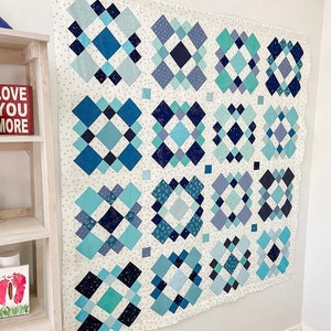 May include: A quilt with a white background and a pattern of blue and teal diamond shapes. The quilt is made up of 16 squares, each with a different diamond pattern.