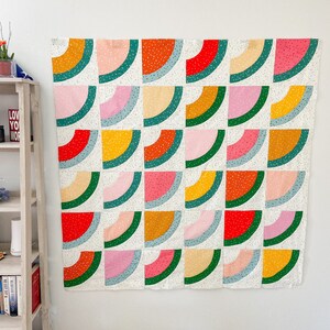 May include: A colorful quilt with a geometric pattern of watermelon slices in shades of red, pink, green, yellow, and white.