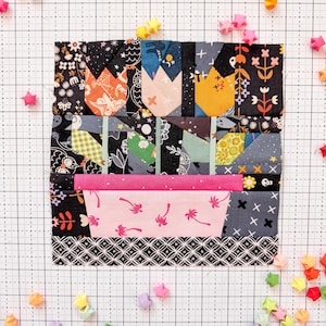 Może przedstawiać: Kolorowy blok patchworkowy z motywami tulipanów w kolorze pomarańczowym, różowym i żółtym, na czarnym tle z kwiatowymi wzorami. Różowy prostokąt z motywami palm znajduje się na dole. Rozrzucone gwiazdki origami dodają zabawnego akcentu.