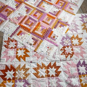 Könnte beinhalten: Zwei handgefertigte Quilts mit Patchwork-Designs. Ein Quilt zeigt quadratische Blöcke mit konzentrischen Rechtecken in Rosa-, Orange- und Lilatönen. Der andere Quilt hat sternförmige Muster in ähnlichen Farben. Beide Quilts befinden sich auf einem weißen Hintergrund.