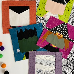 May include: Five different fabric squares with Halloween themes. The squares are made of various fabrics with different patterns and colors, including orange, green, black, white, pink, and blue. The squares are arranged in a staggered pattern on a white surface with a black lace overlay.