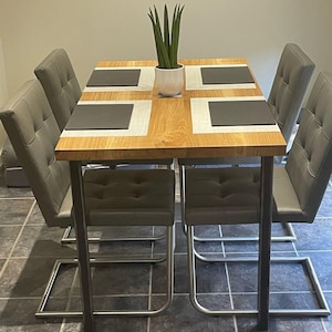 May include: A square wooden dining table with a black metal base and four gray upholstered chairs. The table has four gray placemats and a potted plant in the center.