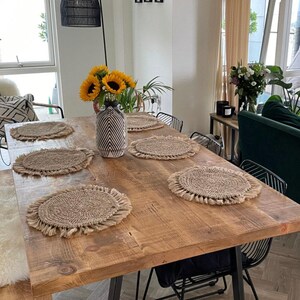 May include: A rustic wooden dining table with six woven placemats and a decorative vase with sunflowers. The table is approximately 72 inches long and 36 inches wide. Black metal chairs surround the table, creating a warm and inviting dining space.