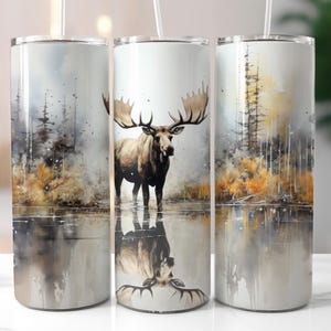 Op de afbeelding: Drie roestvrijstalen bekers met een aquarelontwerp van een eland die in een meer staat met bomen op de achtergrond. De bekers hebben deksels en rietjes.