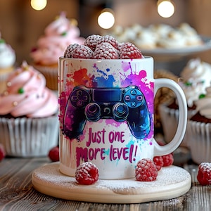 May include: White ceramic mug featuring a video game controller design and the text "Just one more level!" The mug is filled with fresh raspberries and sits on a wooden coaster. The mug has colourful paint splatters.