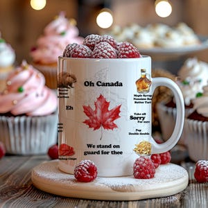 May include: White ceramic mug with a Canadian theme. The mug features a red maple leaf, the words "Oh Canada", and various Canadian icons and phrases. The mug is surrounded by raspberries and powdered sugar.