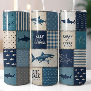 Puede incluir: Un vaso cilíndrico con un diseño de patchwork en tonos azul, crema y blanco. El patrón incluye varias ilustraciones de tiburones, olas, rayas, lunares y el texto "KEEP SWIMMING", "SHARK VIBES" y "BITE BACK" en color azul oscuro.