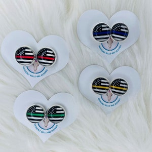May include: Four pairs of heart-shaped earring cards with different colored American flag designs. The cards are white with black text that reads "Heavenly Belle-Rae Designs".
