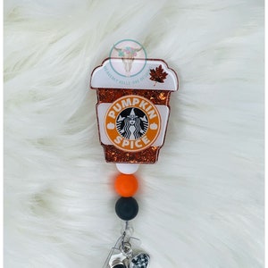 May include: A white and orange pumpkin spice latte themed retractable badge holder with a black and white checkered charm and black and orange beads.