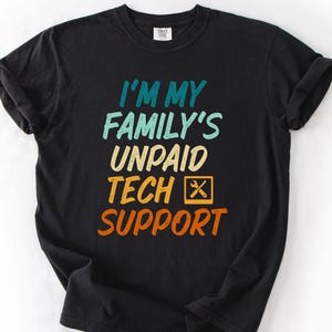 Peut inclure: T-shirt noir avec l'inscription "I'M MY FAMILY'S UNPAID TECH SUPPORT" en turquoise, bleu clair, beige, orange et jaune. Le t-shirt a un col rond et des manches courtes. Le texte est centré sur le devant.