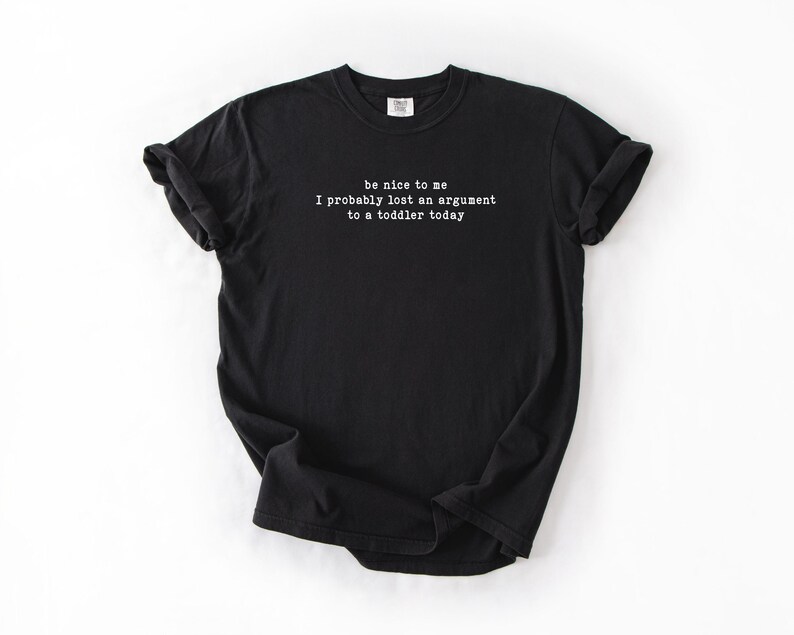 Może przedstawiać: Czarny t-shirt z białym napisem: "be nice to me I probably lost an argument to a toddler today." Koszulka z kr&oacute;tkim rękawem wykonana jest z miękkiego materiału. Koszulka jest prezentowana na białym tle.