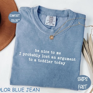Może przedstawiać: Niebieska koszulka Comfort Colors z napisem "be nice to me I probably lost an argument to a toddler today" w kolorze białym. Złoty naszyjnik z wisiorkiem jest na koszulce.