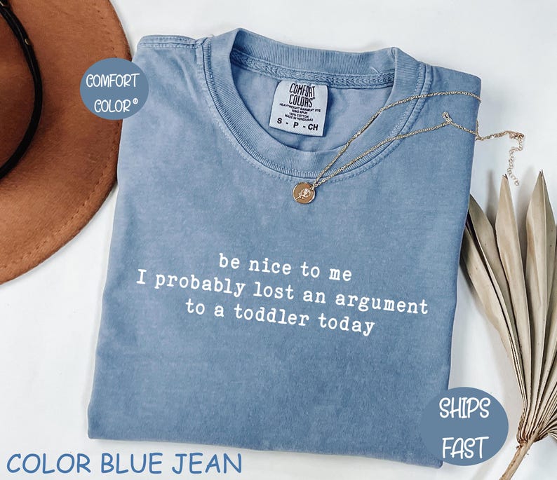 Może przedstawiać: Niebieska koszulka Comfort Colors z napisem "be nice to me I probably lost an argument to a toddler today" w kolorze białym. Złoty naszyjnik z wisiorkiem jest na koszulce.