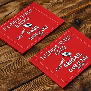 May include: Two red graduation announcements with white text. The top announcement says "Illinois State Bound" and "Congrats! Paul Class of 2027 Finance". The bottom announcement says "Illinois State Grad" and "Congrats! Abigail Class of 2023 Agriculture".