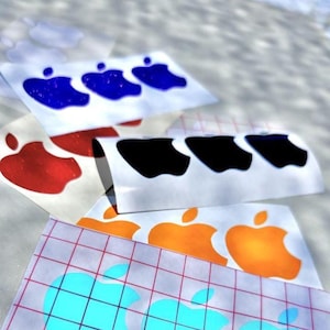 May include: A collection of adhesive vinyl decals featuring the apple logo shape in various colors including blue, red, black, orange, and light blue. The decals are arranged on white backing paper, with some sheets showing a grid pattern.