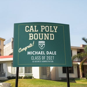 Könnte beinhalten: Ein grünes Schild mit weißem Text, auf dem "Cal Poly Bound" und "Herzlichen Glückwunsch!" in kursiver Schrift steht. Unter dem Text befindet sich ein Wappen mit einem Berg und Werkzeugen. Das Schild enthält auch den Namen "Michael Dale", "Klasse von 2027" und "BS Business Administration".