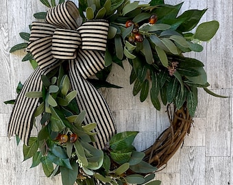 Può includere: Una ghirlanda decorativa con una base di vite naturale, adornata con un rigoglioso fogliame verde, bacche finte e un grande fiocco a righe nere e beige. Adatta per l'arredamento stagionale della casa.