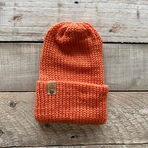May include: A bright orange knitted beanie with a brown leather patch that says "Genuine & Co."