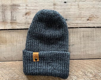 May include: A dark gray knit beanie with a brown leather patch that says "seam & stitch".