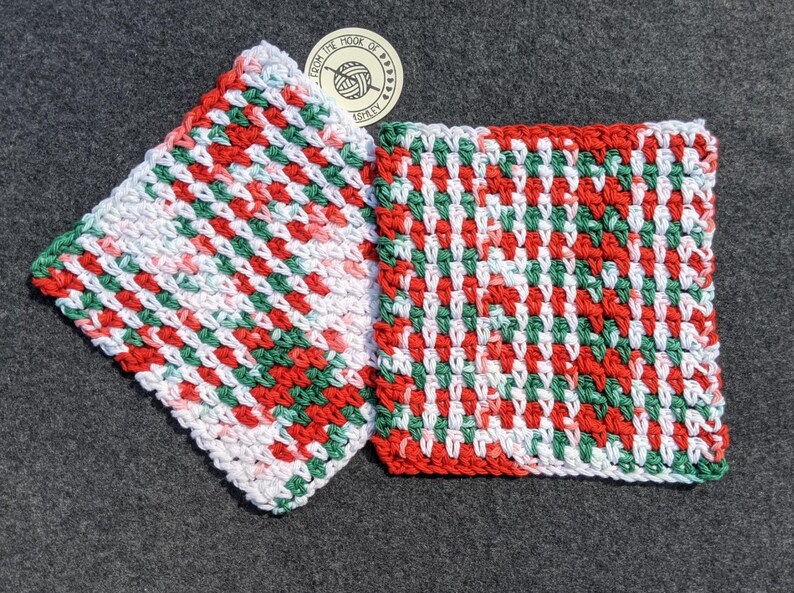 May include: Two handmade, square crochet washcloths. The washcloths feature a repeating pattern of red, green, and white yarn. One washcloth is angled, and the other is flat. A circular tag with text is visible.